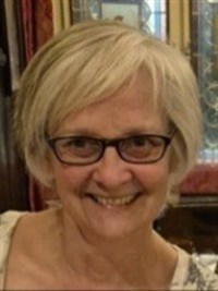 A white woman with short grey hair and glasses is smiling at the camera