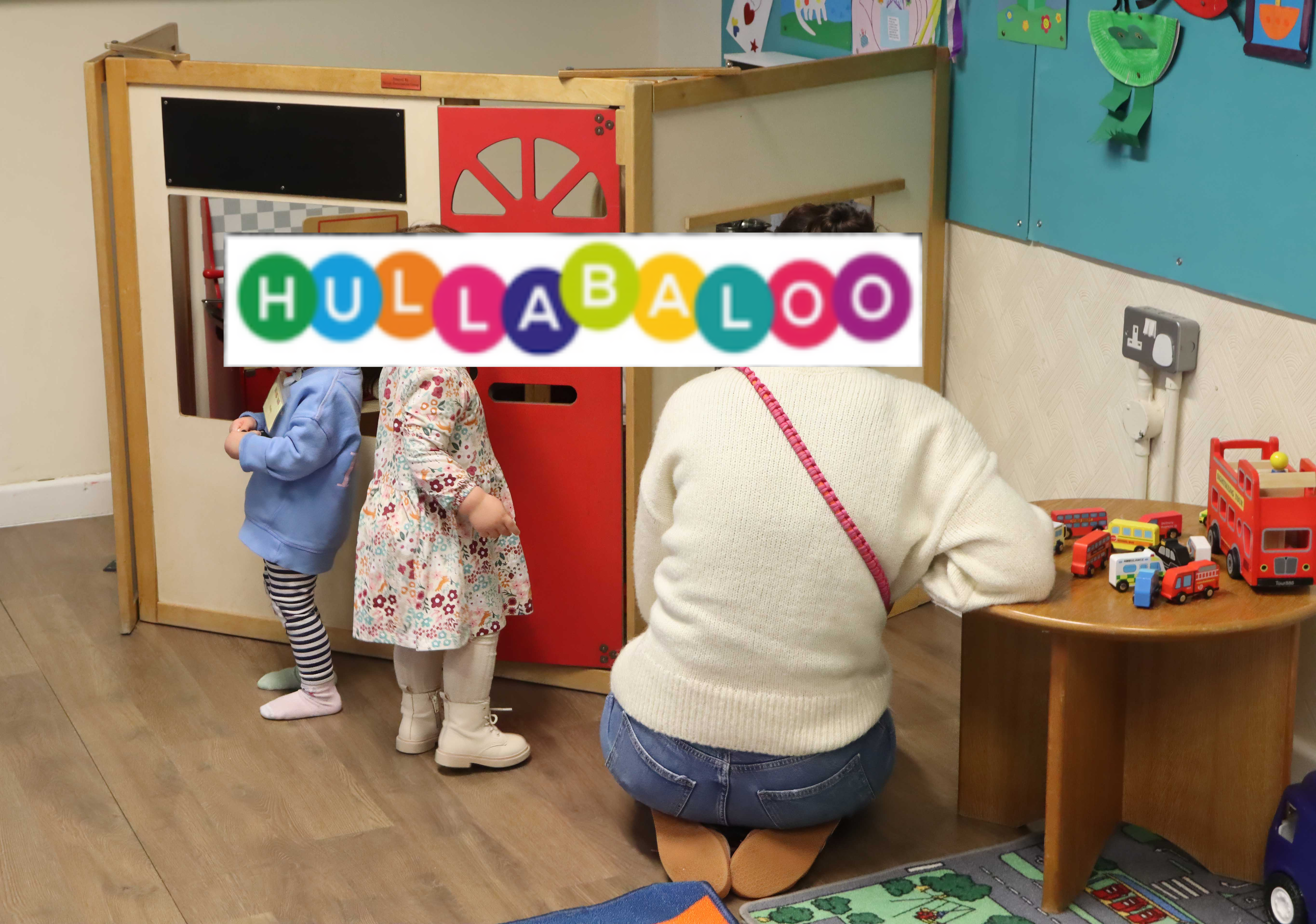 A woman and 2 children playing with a Wendy House. The word 'Hullabaloo' covers their faces