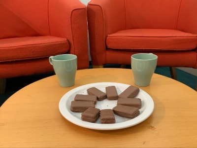 2 comfy red chairs and a coffee table set with tea and biscuits.