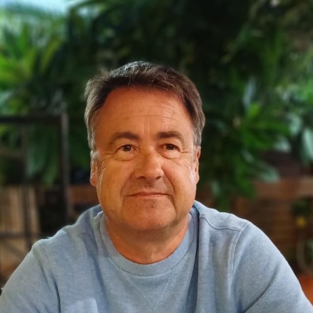 a white man with short dark hair and wearing a grey top looks at the camera