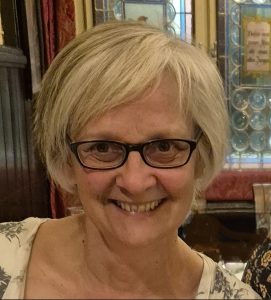 A white woman with short grey hair and wearing glasses is smiling at the camera
